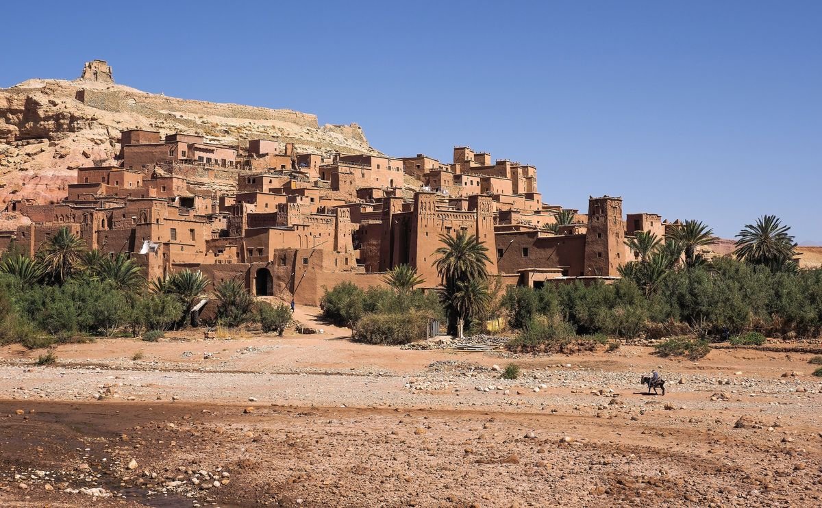 The earthen ksar of Aït Benhaddou rising above palm trees and the dry riverbed of the Ounila valley