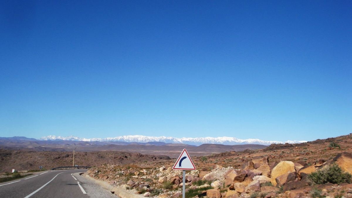 Paved road crossing the stony plateau of Ouarzazate province with the snow-capped High Atlas on the horizon