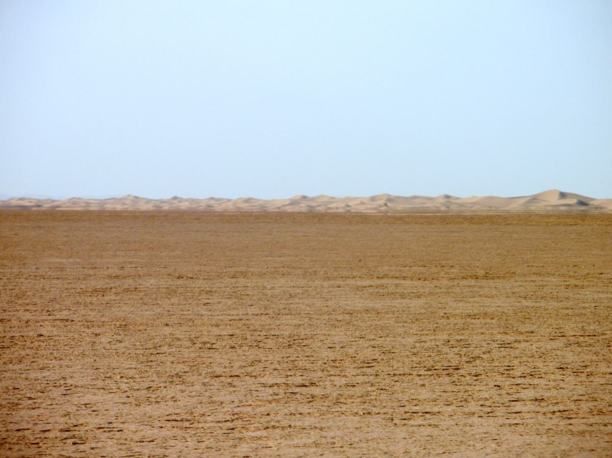 The flat dry bed of Lake Iriqui with a line of dunes on the horizon