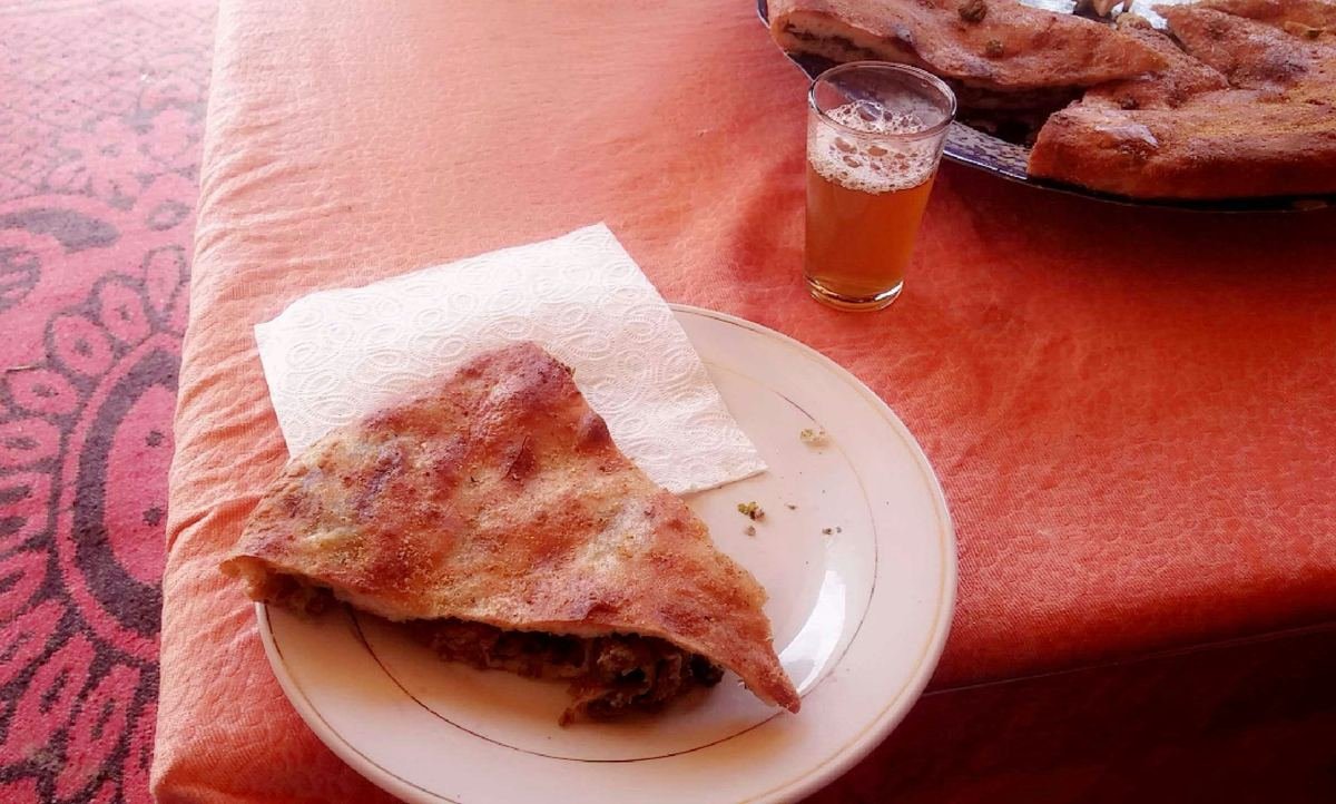 Freshly baked Berber pizza, or madfouna, a slice on a plate with a glass of mint tea