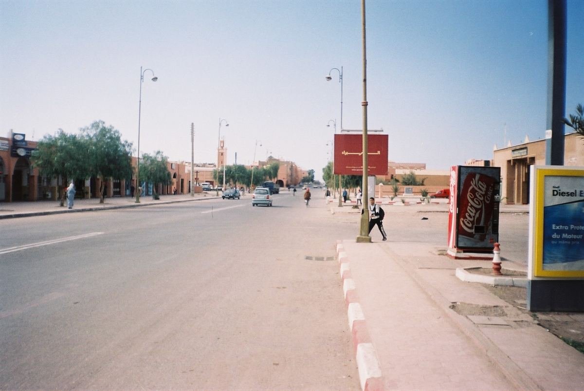 A long straight avenue in Ouarzazate lined with trees, street lamps and low ochre buildings