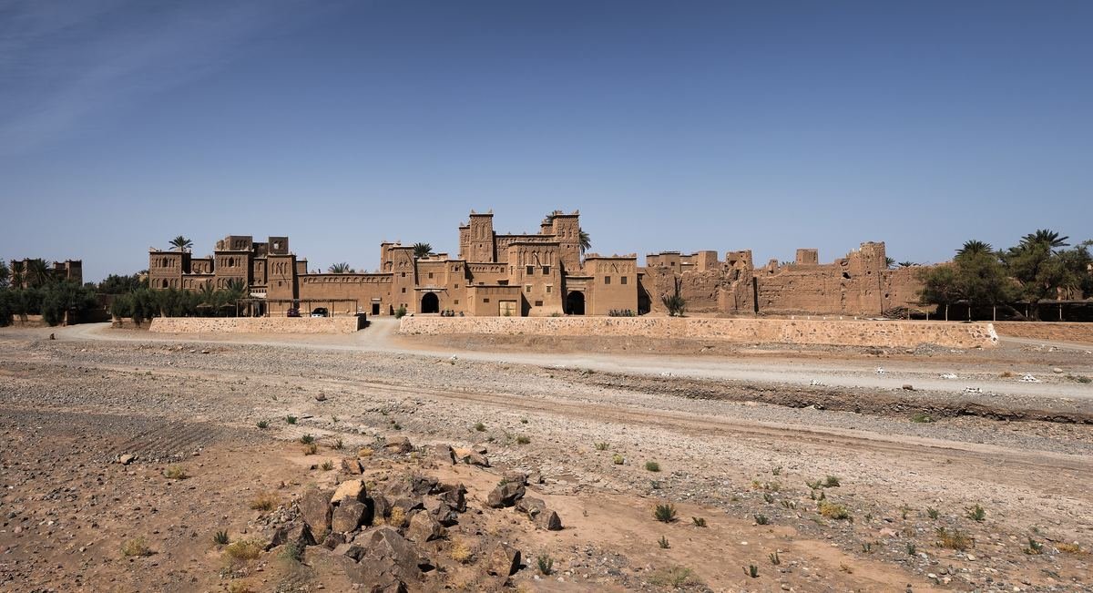Kasbah Amridil seen across the dry riverbed in the Skoura oasis, with palm trees on both sides