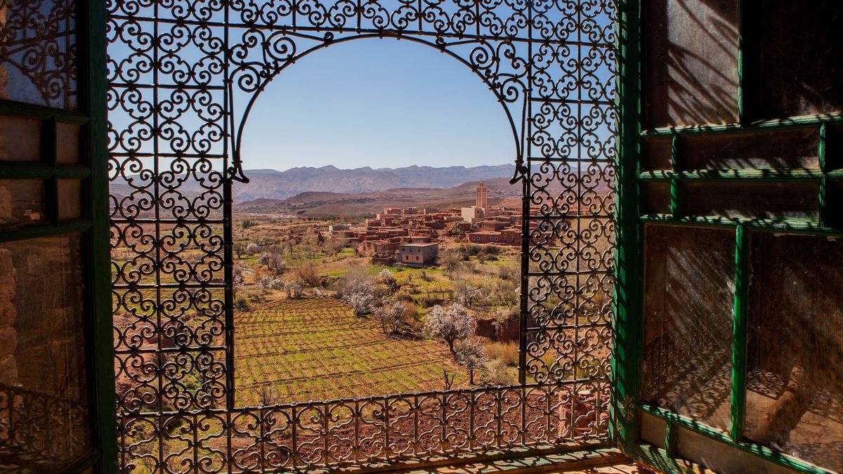 View through a wrought iron window grille of the Telouet kasbah over the village, fields and High Atlas foothills