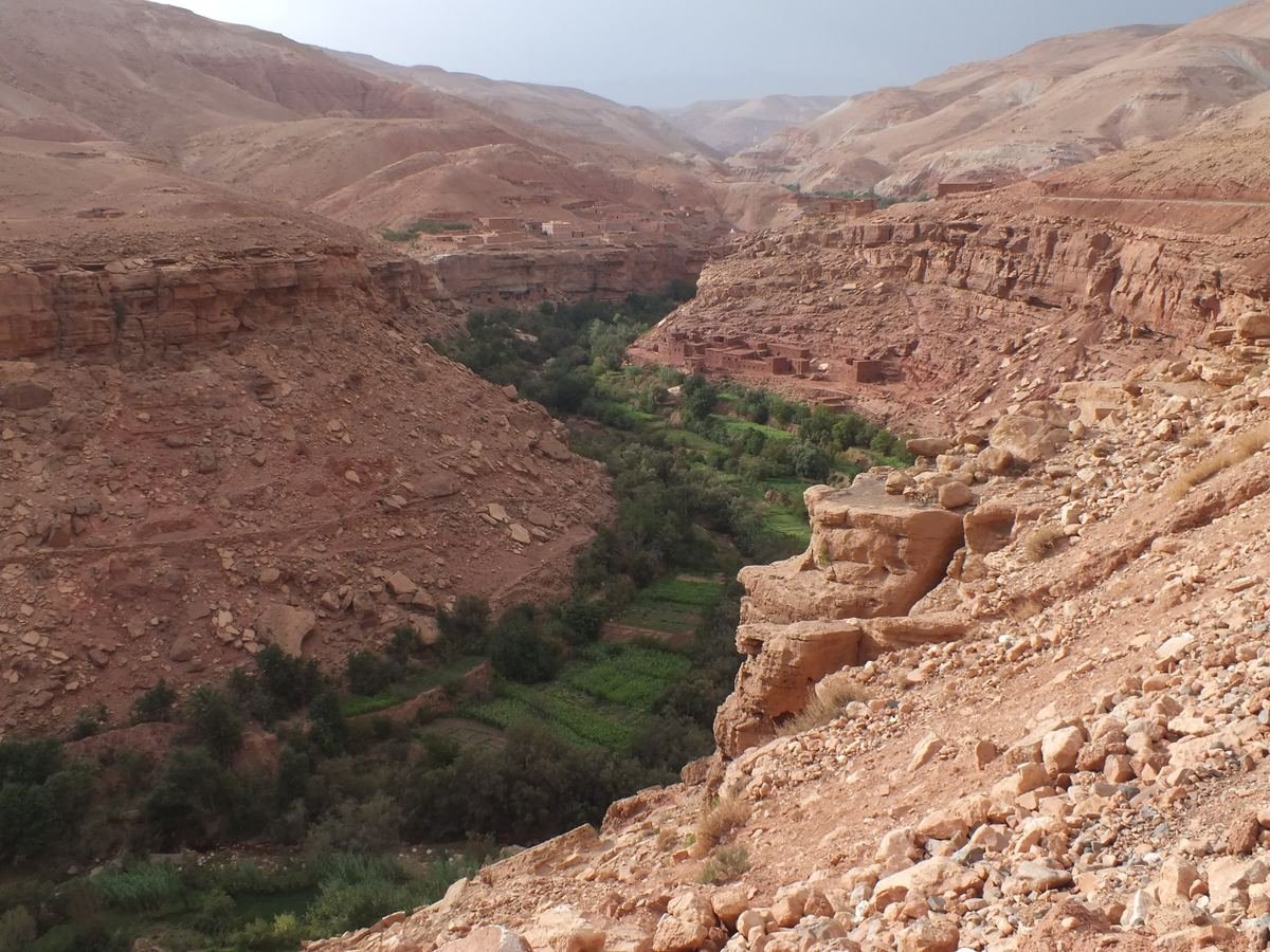 Green fields along the Ounila river at the bottom of a red rock canyon, with earthen villages on the slopes
