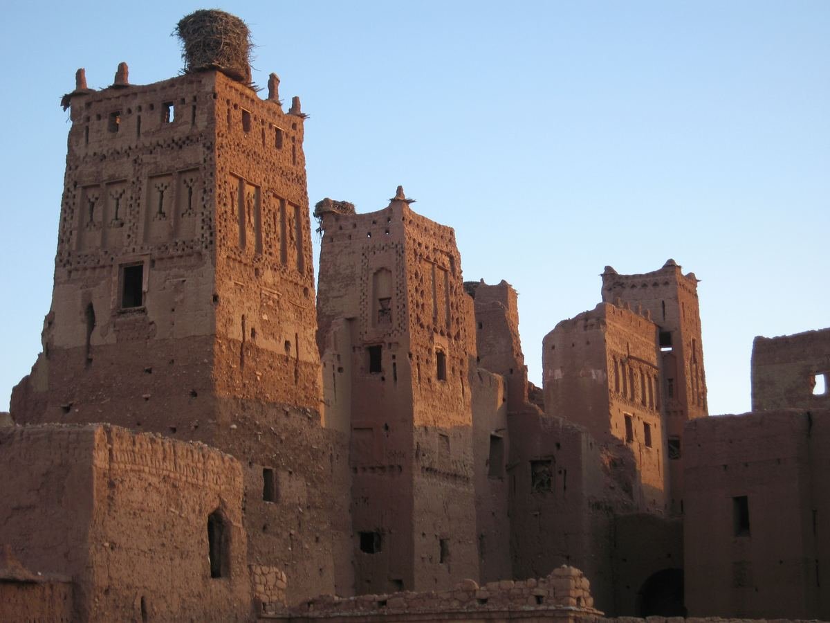 Decorated earthen towers of the Tamdaght kasbah with a stork nest on top, in warm evening light